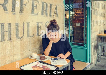 Junge Frau auf der Terrasse einer Bar bei einem Kaffee mit seinem Handy in der Stadt Santander, Kantabrien, Spanien. Stockfoto