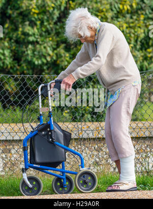 Ältere Dame zu Fuß mit Hilfe einer Gehhilfe mit Rädern, in England, Großbritannien. Rollator oder fahrbare Gehhilfe. Stockfoto