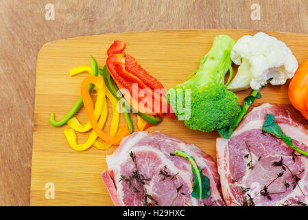 rohes Schweinefleisch in Marinade, auf ein Schneidebrett mit Tomaten auf einem Zweig, ein Messer für Fleisch und Gewürze Grenze, Platz für Text auf wo Stockfoto