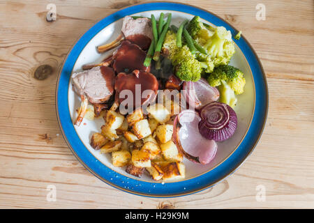 Englisches Abendessen braten Rack Lamm Brokkoli Zwiebeln und Sauce serviert auf einem blau-weißen Platte Holztisch Stockfoto