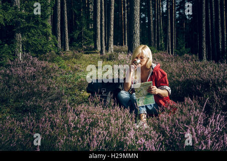 Junge aktive Frau Touristen sitzen auf einer Lichtung im Wald aus einer Thermoskanne Tee zu trinken und auf der Suche nach Karte. Gesunden, aktiven Lebensstil-Konzept. Stockfoto