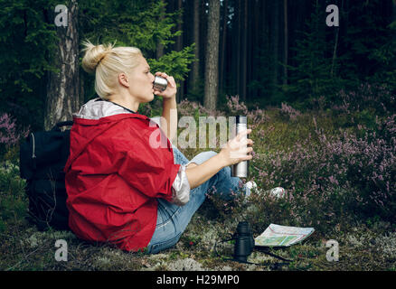 Junge aktive Frau Tourist aus einer Thermoskanne Tee trinken und sitzen in den Wald. Tourismus. Gesunden, aktiven Lebensstil-Konzept Stockfoto