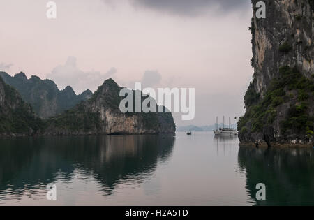 Dschunke und Fischerboot zwischen Karstgebirge im Morgengrauen in Halong Bucht, Vietnam Stockfoto