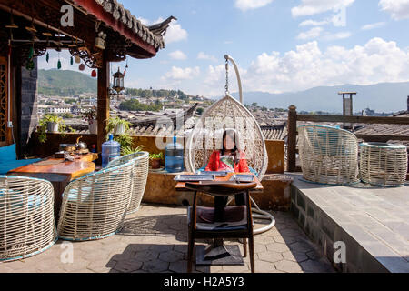 Orientalische Frau Touristen Entspannung in Ei-Sessel auf der Dachterrasse mit Blick über Lijiang in China Stockfoto