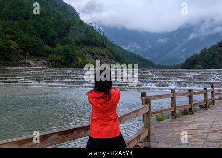 Frau touristischen Blick auf cascading Wasser und Nebel bedeckt Berge in Yunnan, China Stockfoto