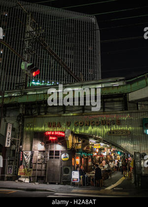 Tokyo nach Einbruch der Dunkelheit. Yamamote-Line-Zug auf erhöhten Schienen über dem belebten Restaurants mit Gönnern an Straße Tabellen. Gaado-Shita, Yurakucho, Tokyo, Japan Stockfoto