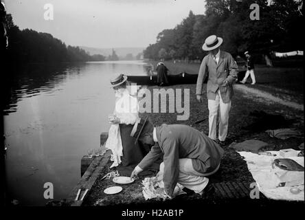 Picknick auf der Themse... Waschen danach Gläser und Teller. Eine junge Frau und zwei Männer in Bootsfahrer hüten. Beachten Sie die Zeitung und Gurke im Vordergrund. C1910.  Foto von Tony Henshaw. Stockfoto