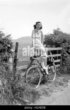 Eine junge Frau posiert mit ihrem Fahrrad-c1935 auf ein Tor. Eine schöne Pose gekleidet in stilvollen Strickmode mit schöne gleichmäßige Ausleuchtung. Foto von Tony Henshaw Stockfoto