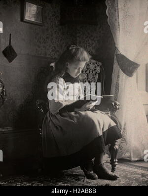 Atmosphärische fotografische Studie eines Mädchens mit natürlichem Licht zu lesen. Amateur Familienfotos c1899 scheint Ort Hastings. Foto von Tony Henshaw.  Entnommen aus frühen Original Glas-Folien (positive Originalbilder). AUS DER FAMILIENSAMMLUNG 1899 HASTINGS Stockfoto