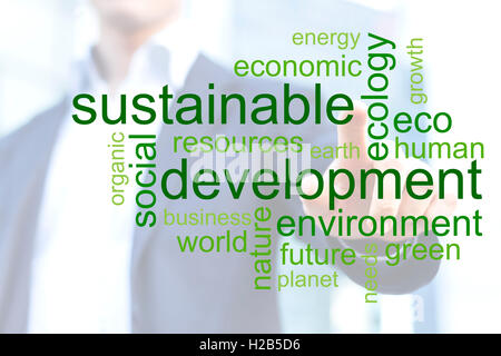 Geschäftsmann berührt grüne tagcloud über nachhaltige Entwicklung mit Bürogebäude im Hintergrund Stockfoto