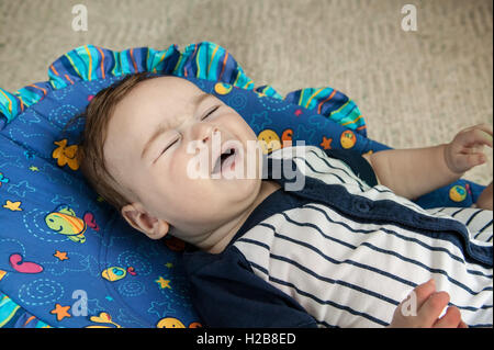 Unglücklich vier Monate altes Babyjungen Weinen liegen in einem Schaukelstuhl Sitz abgeholt werden wollen Stockfoto