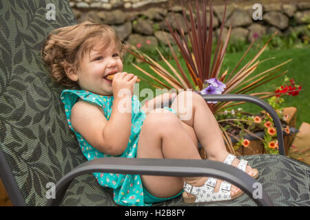 Achtzehn Monate altes Mädchen essen ein Müsliriegel außerhalb mit ihrer Mutter neben ihr, in Issaquah, Washington, USA Stockfoto