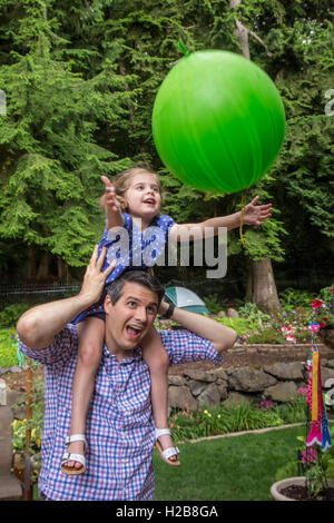 Dreißig vier Jahre alten Vater hält seine dreijährige Tochter, wie sie einen Ballon warf ihr Fänge Stockfoto