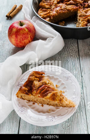 Stück hausgemachten süßen Apfel und Zimt Kuchen auf Vintage weißen Teller. Pie in eine Auflaufform und frisches Obst auf hölzernen Hintergrund. Stockfoto
