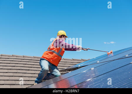 junge Arbeitnehmer Reinigung Solarzellen auf Hausdach Stockfoto