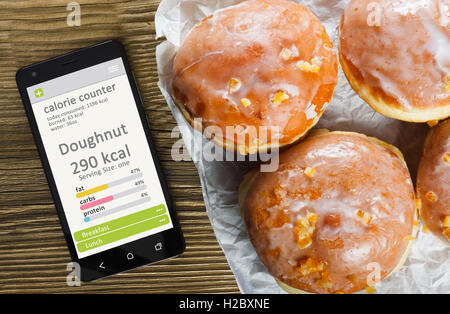 Kalorien-Zähler Konzept - Handy mit Kalorien-Zähler-app auf dem Bildschirm und Krapfen. Holztisch als Hintergrund Stockfoto