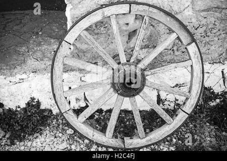 Alte hölzerne Rad steht in der Nähe von Stein ländlichen Wand, schwarz / weiß Retro-Stil Foto Stockfoto