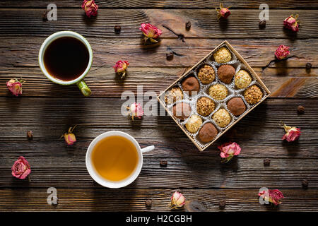 Süße Speisen Muster. Schachtel Pralinen, Kaffeebohnen, trocken rose Blumen, Tasse schwarzen Kaffee und grünem Tee auf Holztisch Stockfoto