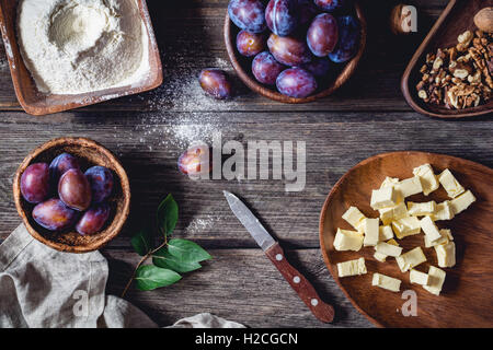 Zutaten für Plum Pie: frische Pflaumen, Walnüsse, Mehl mit Zucker und gehackten Butter auf rustikalen Holztisch. Draufsicht Stockfoto