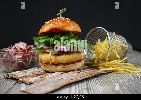 Fishburger auf die Holzplatten mit Käse, Gurke, Zwiebel, grüne und rote Salat und Pommes Frites. Stockfoto