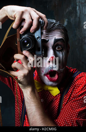 Der gruselige Clown und eine Kamera auf Dack Hintergrund. Halloween-Konzept Stockfoto