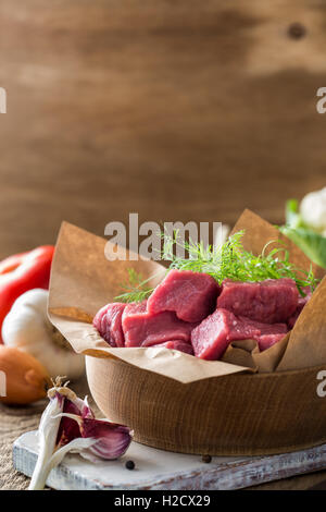 Rohes Kalbfleisch mit Gemüse und anderen Zutaten bereit, auf rustikalen Holztisch, Bio-Koch-Konzept Kochen in Stücke geschnitten Stockfoto