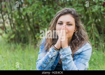 Porträt von Brünette Teenager-Mädchen im Freien zu sitzen. Das Mädchen hat ihre Hände vor ihr Gesicht. Stockfoto