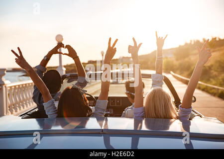 Gruppe von glücklichen jungen Freunden im Cabriolet mit erhobenen Händen auf Sonnenuntergang fahren Stockfoto