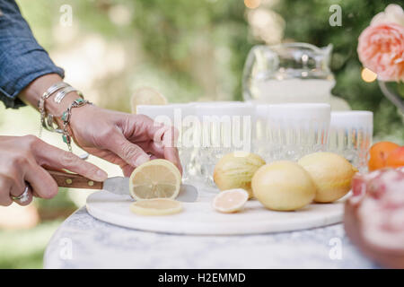 Nahaufnahme einer Frau an einem Tisch im Garten stehen, schneiden Zitrone s für einen Drink. Stockfoto