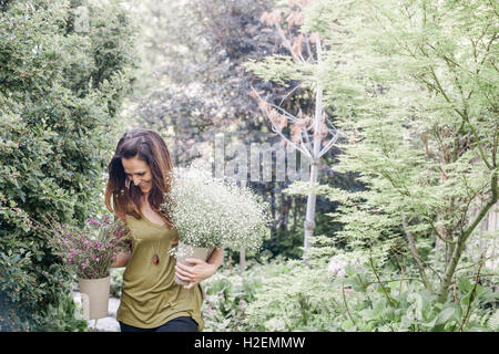 Frau zu Fuß durch einen Garten mit einem großen Blumenstrauß. Stockfoto