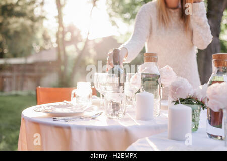 Frau einrichten einen Tisch in einem Garten, Kerzen und eine Vase mit rosa Rosen. Stockfoto