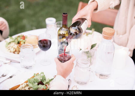 Nahaufnahme von einem einen Tisch mit Speisen und Getränken in einem Garten, Frau, gießen ein Glas Rotwein. Stockfoto