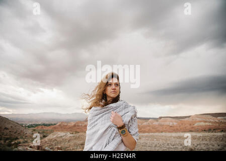 Eine Frau mit vom Wind verwehten Haaren eingewickelt in ein Tuch in eine Wüstenlandschaft Stockfoto