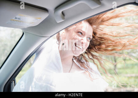 Frau auf einem Roadtrip, schiefen aus einem Autofenster, Lon g rote Haare im Wind wehen. Stockfoto