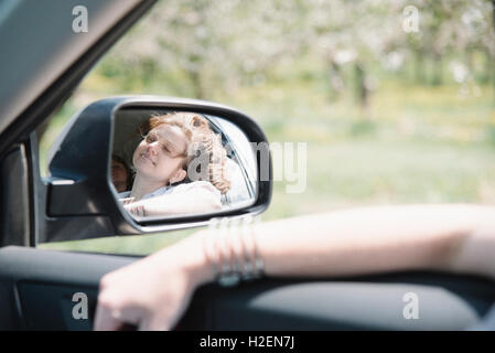 Frau in einem Auto auf einem Road-Trip, Blick aus Fenster, Reflexion in den seitlichen Spiegel. Stockfoto