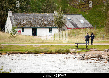 Zwei Besucher im Herbst warm anziehen, wie Sie Bilder von Loch ein Eilein vom Ufer des Loch mit Besucherzentrum hinter Ihnen, Rothiemurchus Estate, Rothiemurchus, Schottland, Großbritannien Stockfoto