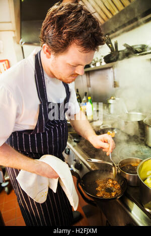 Dorf-Gasthaus-Küche. Ein Koch arbeitet rührende Zutaten in einer Pfanne erhitzen. Stockfoto