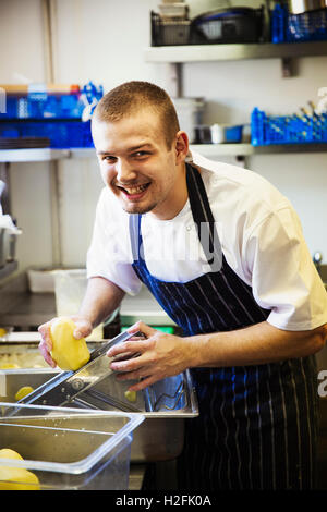 Eine Dorf-Gasthaus-Küche. Ein Koch Schürze zu arbeiten, mit einer Mandoline Cutter auf Kartoffeln. Stockfoto