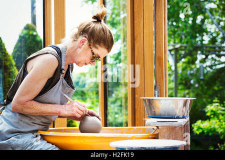 Eine Frau Töpfer arbeiten Ton auf einer Töpferscheibe in ihrer Werkstatt. Stockfoto