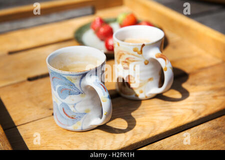 Zwei Tassen und einen Teller mit Obst auf einem Gartentisch. Stockfoto