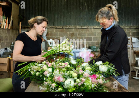 Kommerzielle Blumenbinden. Zwei Frauen an einer Werkbank erstellen floral Tisch Dekoration s und Arrangements. Stockfoto