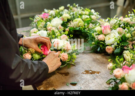 Kommerzielle Blumenbinden. Ein Blumengeschäft, eine Frau arbeitet an einem Blumenschmuck an einer Werkbank. Stockfoto
