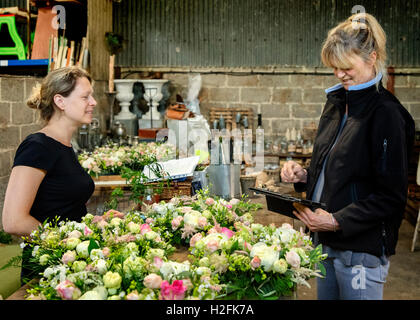 Zwei Frauen, eine mit einer digitalen Tablette. Floristen an einer Werkbank Tisch Dekoration, rosa und weiß Blumenarrangements. Stockfoto