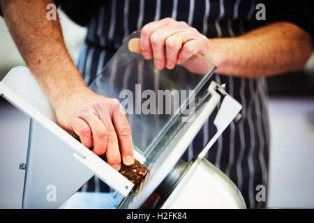 Nahaufnahme eines Metzgers trägt eine gestreifte blaue Schürze, Salami mit einem Hobel schneiden. Stockfoto