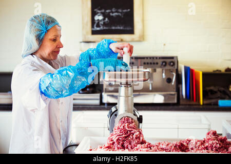 Frau arbeitet in einer Metzgerei, tragen von Schutzkleidung und Handschuhe, einen Fleischwolf Hackfleisch Inbetriebnahme. Stockfoto
