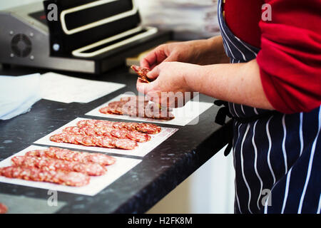 Nahaufnahme eines Metzgers trägt eine gestreifte blaue Schürze Verpackung Scheiben Salami. Stockfoto