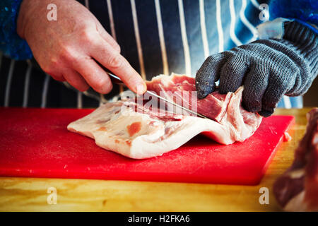 Metzger trägt einen gestreiften blaue Schürze und Schutzhandschuh, Fleisch schneiden. Stockfoto