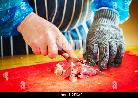 Metzger trägt einen gestreiften blaue Schürze und Schutzhandschuh, Fleisch schneiden. Stockfoto