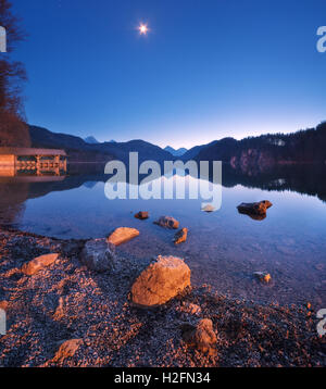 Alpsee See in Deutschland in der Nacht im Frühjahr. Schöne Nachtlandschaft mit See, Berge, Wald, Sterne, Vollmond, Himmel und sto Stockfoto