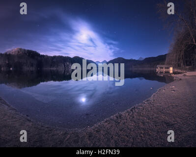 Bunte Nacht-Landschaft mit See, Berge, Wald, Sterne, Vollmond, lila Himmel und Wolken spiegeln sich in Wasser. Frühlingsnacht Stockfoto